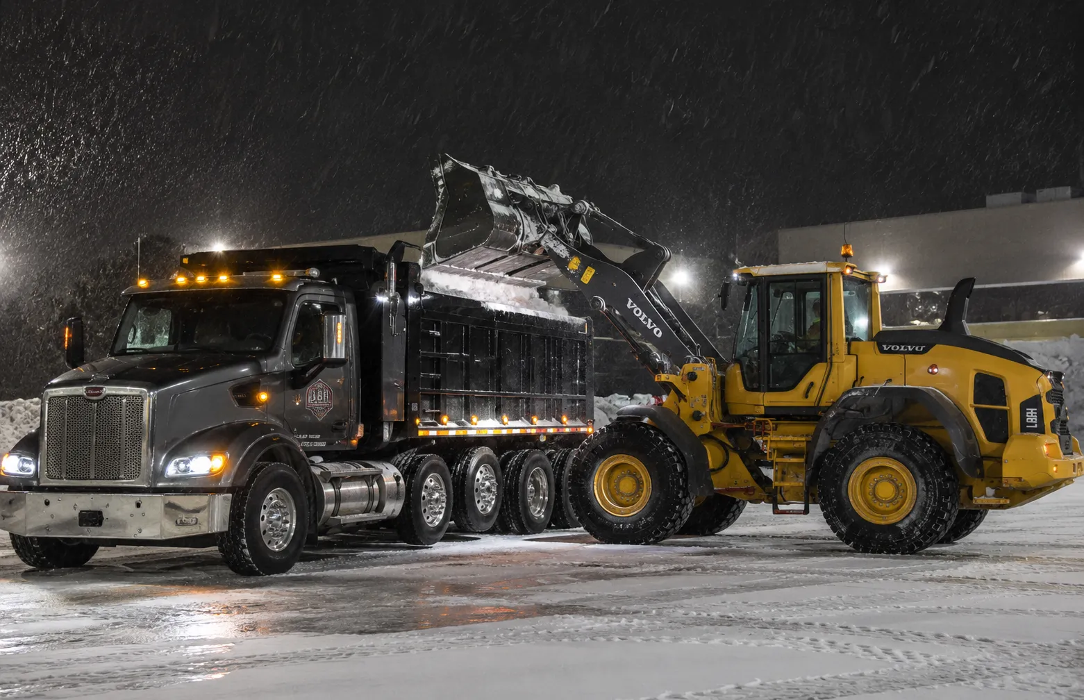 Volvo wheel loader loading snow into a dump truck for off-site hauling in a commercial parking lot in Fond du Lac, WI