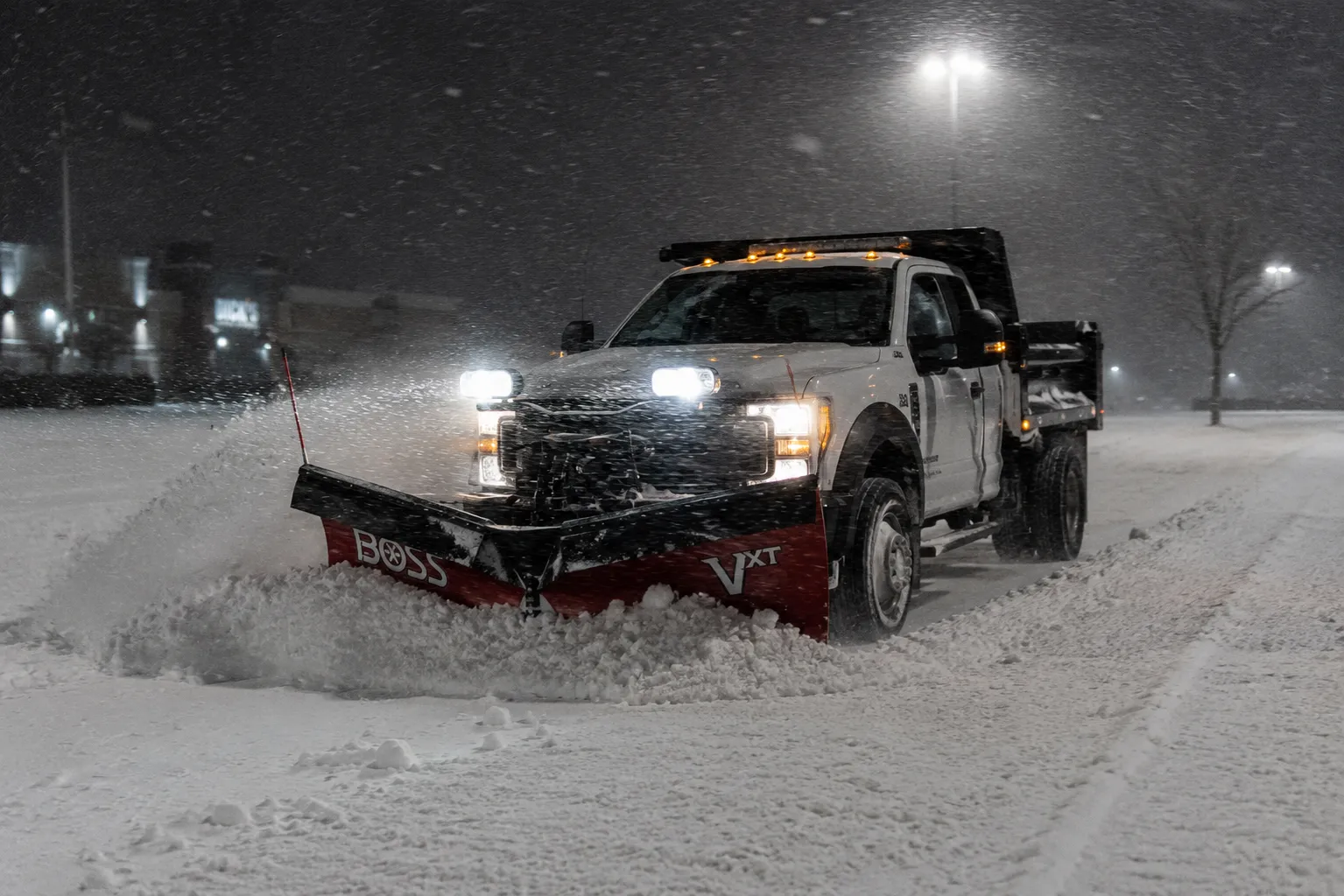 A plow truck clearing a commercial parking lot at night in Fond du Lac, WI